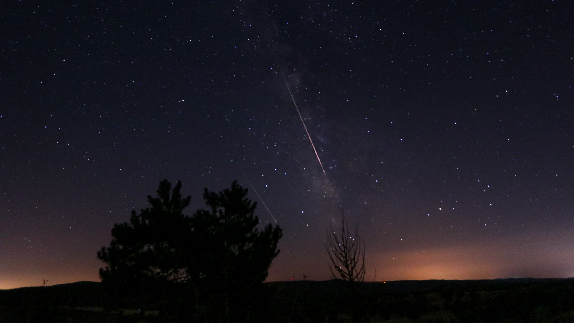 Bright Perseid meteor streaking across a dark star-filled sky above a silhouetted horizon