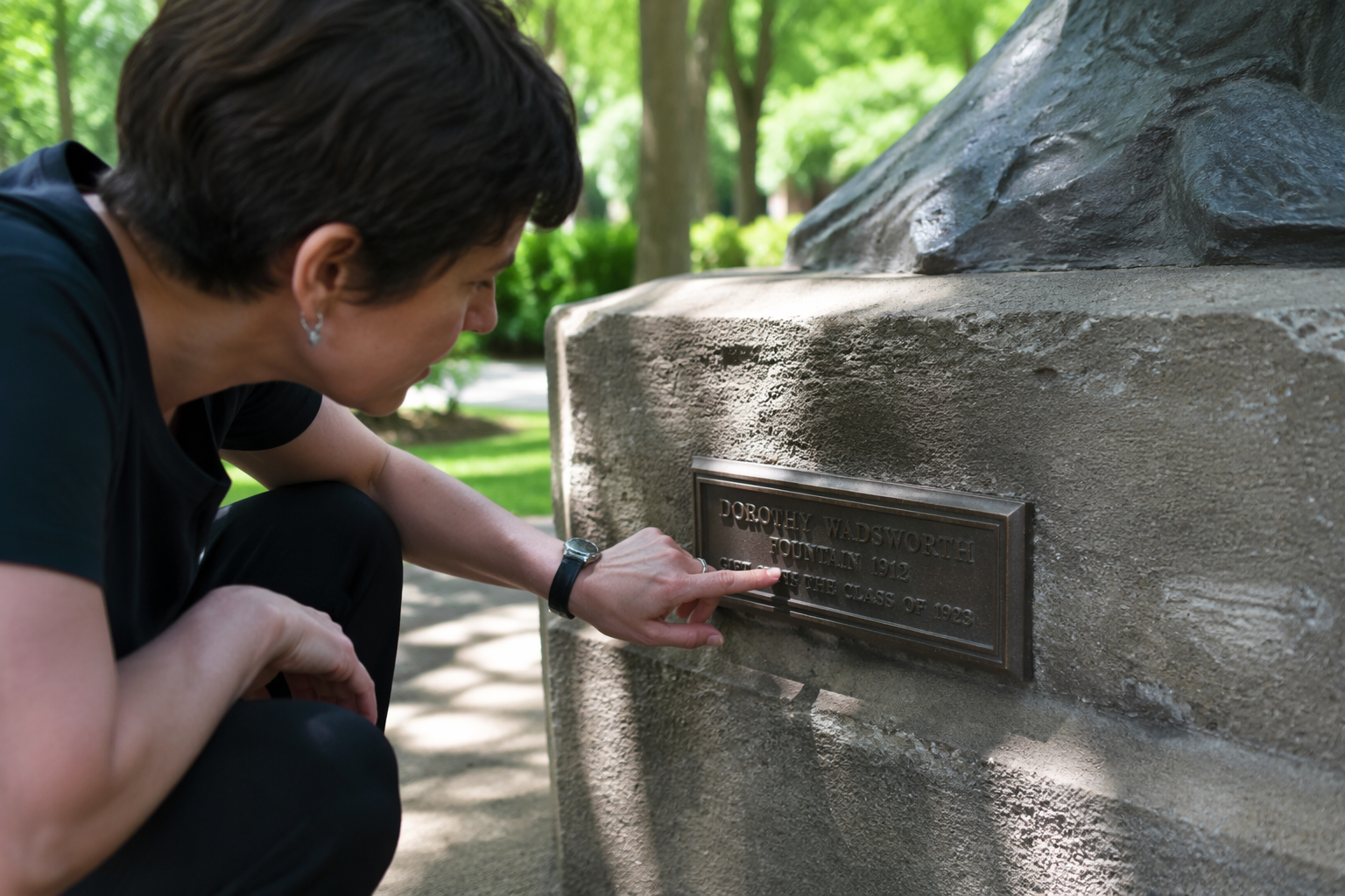 Person reading a bronze plaque on the stone base of a public sculpture