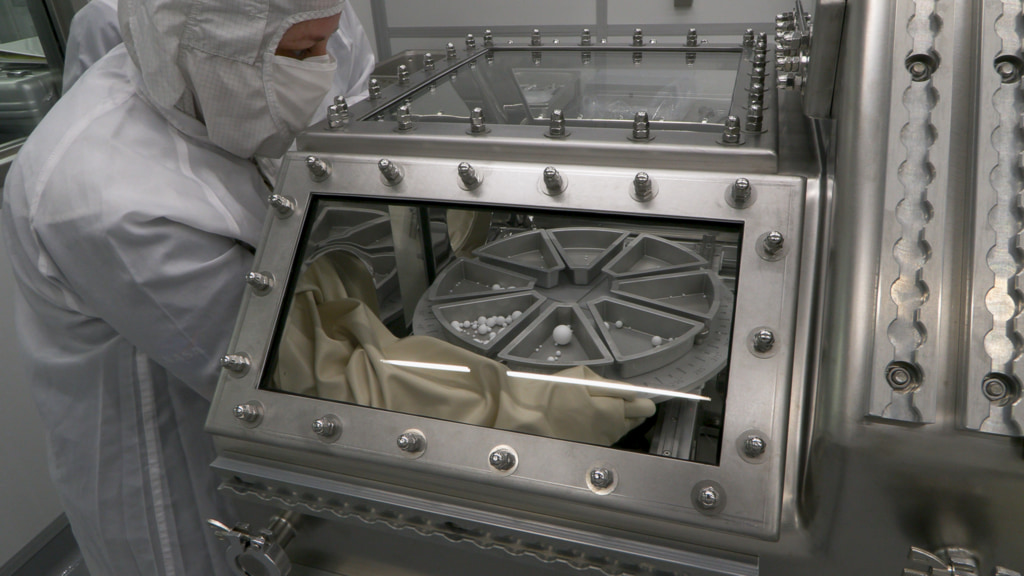 Scientists in clean room suits handling the OSIRIS-REx Bennu sample canister inside a nitrogen-purged glove box
