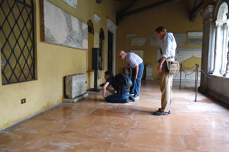 Professor Steven Tuck examining carved Latin inscriptions on a stone block at an archaeological site