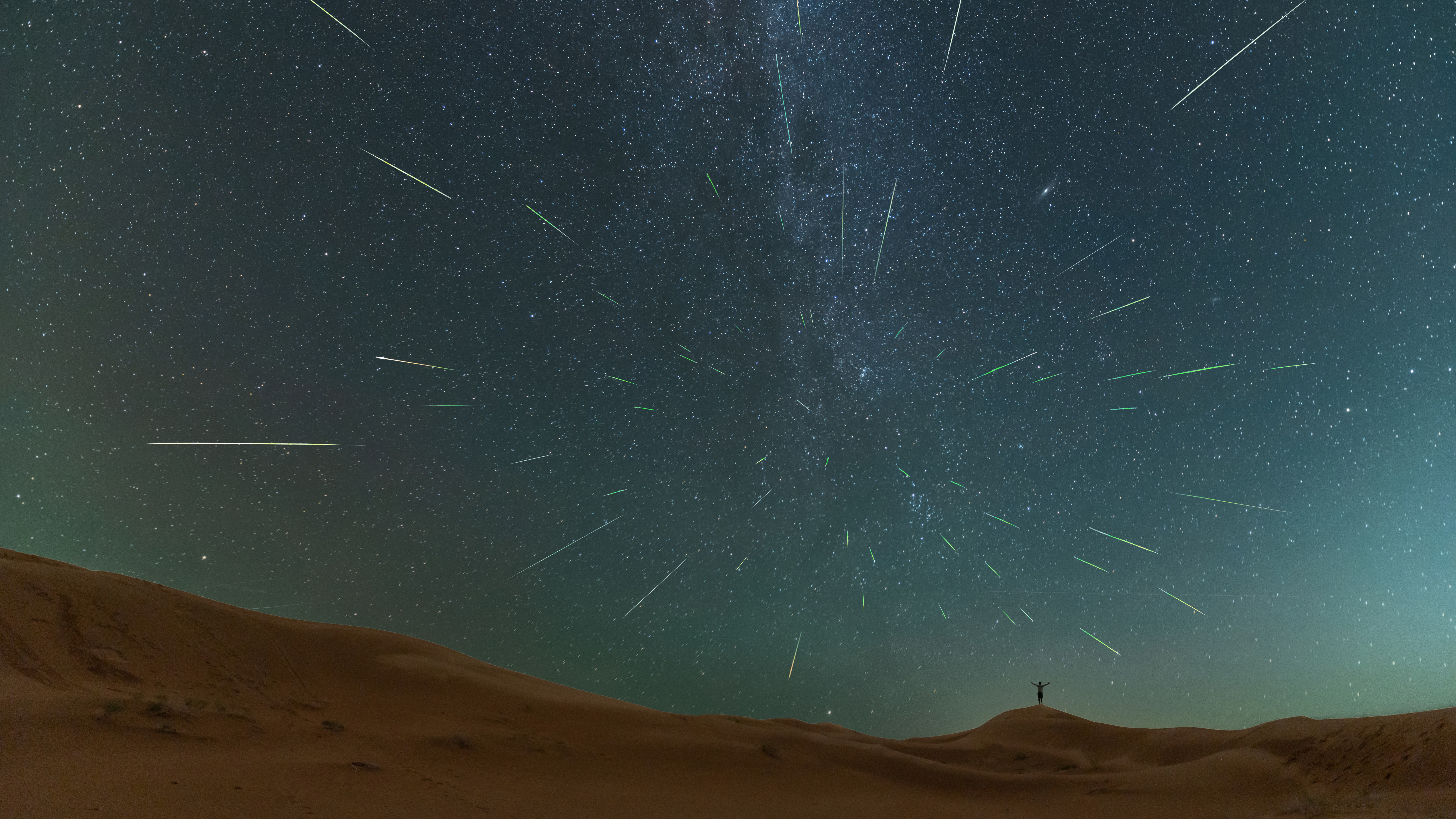 Bright Perseid meteor streaks crossing a dark star-filled sky above a low landscape horizon