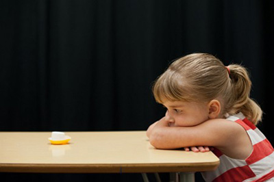 A young girl at a table reaching toward marshmallows during a delay-of-gratification experiment