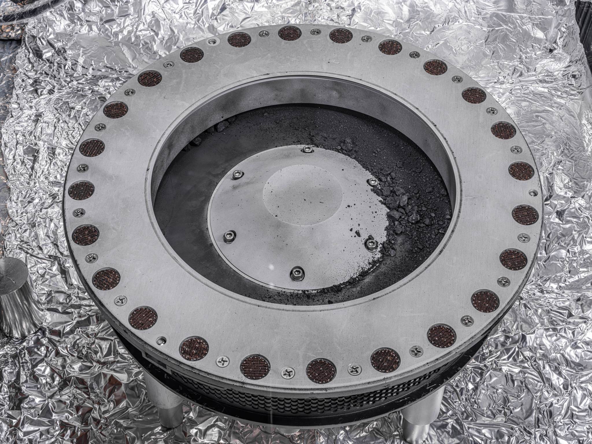 Asteroid Bennu regolith and pebbles on the OSIRIS-REx TAGSAM sampling head in a NASA clean room