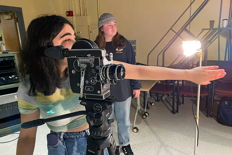A UWM film student framing a shot through a vintage camera on a production set